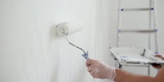 英俊成熟的男人在公寓里修理。那个人用滚筒把墙刷成白色。做你自己。DIY。