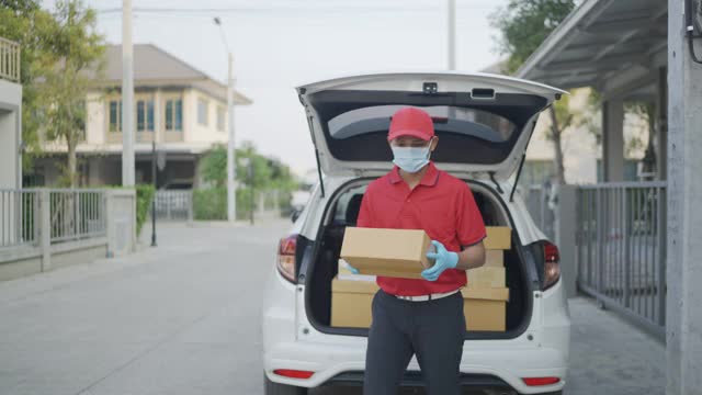 4 k慢动作视频。一名身穿红色制服的男性快递员一边送包裹一边看着摄像头。新标准的概念。