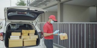 4 k慢动作视频。穿着红色制服的男性快递员寄包裹盒子喷上清洁酒精然后把包裹放在屋前的篱笆上。新标准的概念。