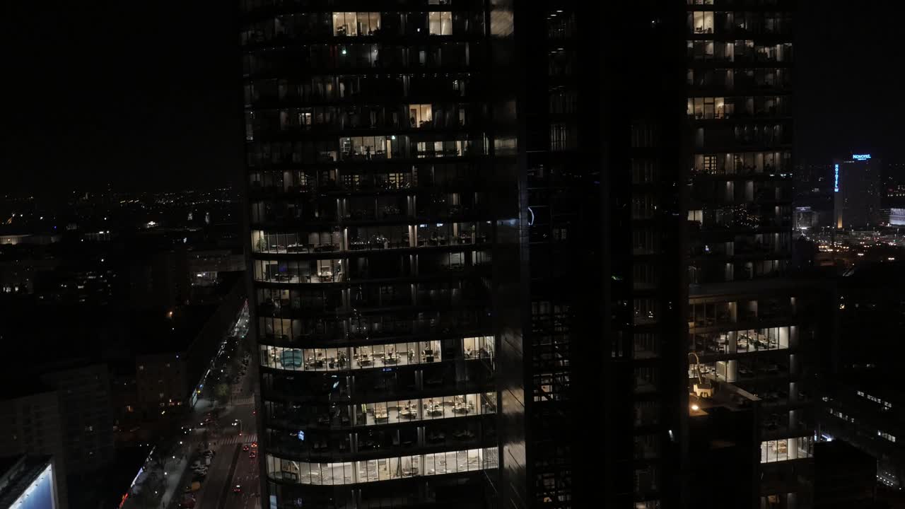 华沙市中心玻璃办公大楼的夜间航拍视频。灯火通明的窗户和倒影。