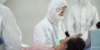 一群身穿防护服的亚洲医生正在医院隔离病房的病床上检查和治疗因冠状病毒或covid - 19咳嗽的患者。流感爆发