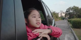4K亚洲小女孩在车里找东西。早上，女孩在上学的路上看着车窗外的东西。孩子们在车里可以看到街景，放松心情。家庭在汽车概念。
