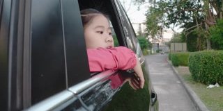 4K亚洲小女孩在车里找东西。早上，女孩在上学的路上看着车窗外的东西。孩子们在车里可以看到街景，放松心情。家庭在汽车概念。