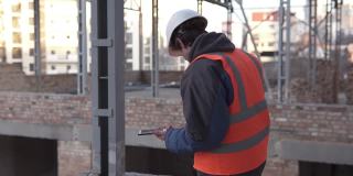 一名头戴白色头盔、手持智能手机的工头正在建筑工地工作。建筑测量和建筑重建。