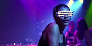 自信的女人，戴着发光的LED眼镜，在夜总会随着电子音乐跳舞。