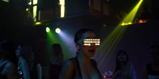 自信的女人，戴着发光的LED眼镜，在夜总会随着电子音乐跳舞。