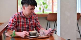 4K年轻的亚洲男子用智能手机查看电子邮件，喝咖啡