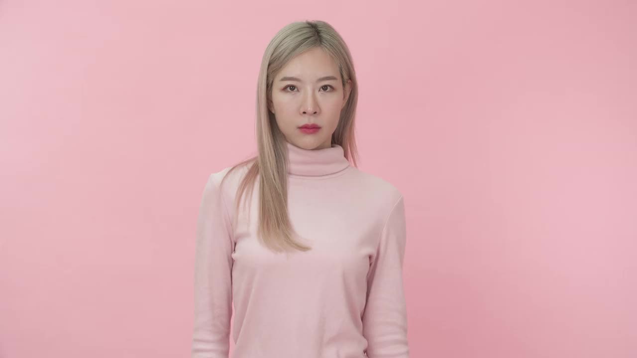 工作室肖像的年轻美丽的亚洲妇女在粉红色的长袖t恤显示停止或否认标志和说不与不高兴的脸在粉红色的背景相机。情感和身体语言的概念。