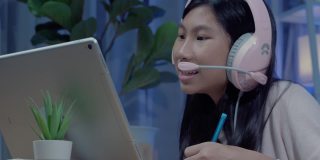 快乐的亚洲女孩使用耳机和麦克风通过数字平板电脑与她的老师和朋友交流，在COVID-19期间在家教育，社交距离概念。