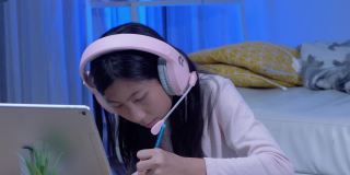 快乐的亚洲女孩使用耳机和麦克风通过数字平板电脑与她的老师和朋友交流，在COVID-19期间在家教育，社交距离概念。
