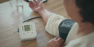 一位老年妇女正在家中用数字压力表测量自己的血压和心率。