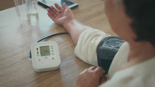 一位老年妇女正在家中用数字压力表测量自己的血压和心率。视频素材模板下载