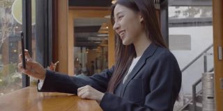迷人的年轻亚洲女子在咖啡店用智能手机视频通话