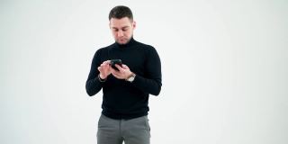 有创意的商人正在研究智能手机。英俊的男子在黑色毛衣使用手机孤立在白色演播室背景。