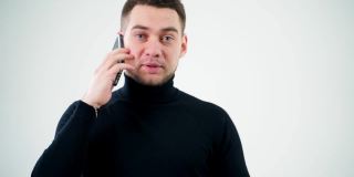 一个帅哥打电话的肖像。在白色的演播室背景下，穿着黑色毛衣的严肃男子正在用手机说话并给出一些指示。