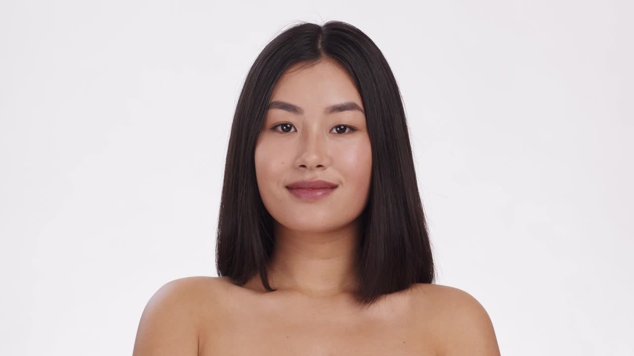 年轻的亚洲女士用棉垫洗脸，微笑着对着镜头，白色的工作室背景，慢镜头