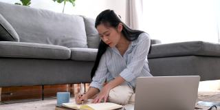 年轻的亚洲女商人正在笔记本上写一个新的项目。她累了，伸懒腰，躺在客厅的沙发上。在家工作，商业女性和工作理念。