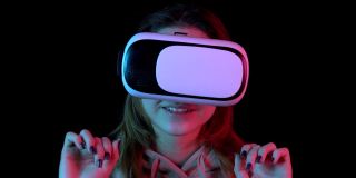 年轻女子在虚拟现实眼镜的特写。一个沉浸在虚拟现实中的女人用手做动作。蓝色和红色的光落在一个黑色背景上的女人身上。