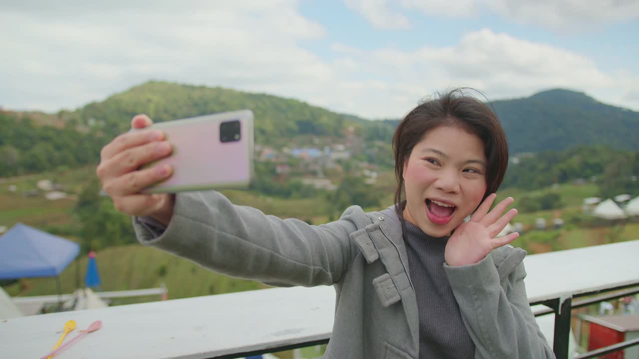 幸福亚洲女性旅行者手用智能手机自拍与欢笑微笑愉快与背景山丘陵自然农场漫步独自旅行的概念