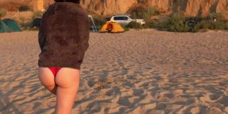 日落时分，一个女人在海滩边用毛巾擦干身体