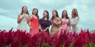 一群美丽迷人的亚洲女性朋友穿着休闲服装站在一起聊天，在红花农场晴朗的天空背景下旅行的概念