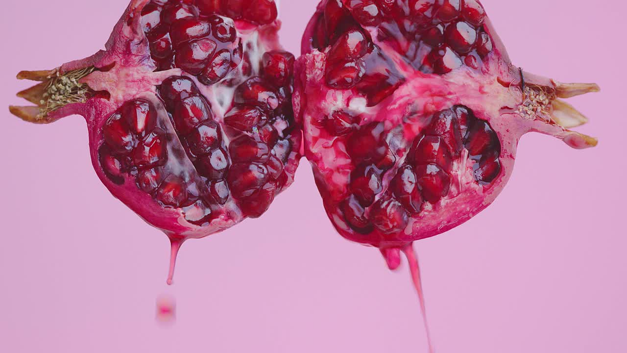 果汁流下来的一半天然红石榴水果在粉红色的工作室背景，健康的饮食理念