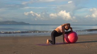 健康的亚洲美女早上在海滩上用球做瑜伽练习。视频素材模板下载