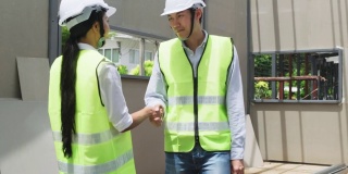亚洲结构工程师和工人在建筑工地握手。所有人在建筑工地行走时须戴上安全帽。商业交易、并购概念