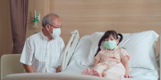 亚洲男医生带着口罩来到康复室，向躺在病床上的儿童病人询问健康问题。男医生检查心率、脉搏和提供健康保健咨询。