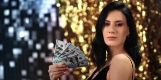 诱人的女人现金美元的钱在银色的金色闪光bokeh。由RED Raven 4k电影摄像机拍摄