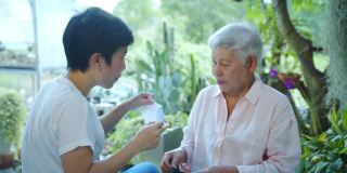 中镜头，慢动作-一个快乐漂亮的亚洲资深妇女试图戴口罩的指导方针从她的照顾。快乐的退休生活。老年人的生活方式和保健理念。