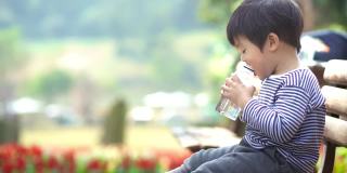 亚洲男婴在公园长凳上喝水