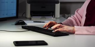 一个年轻女子的手在办公室敲击电脑键盘的特写