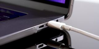 手插入USB类型C线到笔记本电脑的特写镜头在黑色的桌子背景。灰色笔记本电脑上的快速充电类型接口。连接端口上电。暗环境灯光工作室。