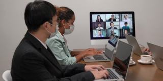 年轻的亚洲团队和资深的办公室员工，员工团队拥有Zoom视频电话通过电脑，商务人士共享桌子使用电脑共同工作