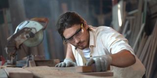木匠木材厂车间桌子上工人用砂纸摩擦木材的特写。做手工的帅哥。