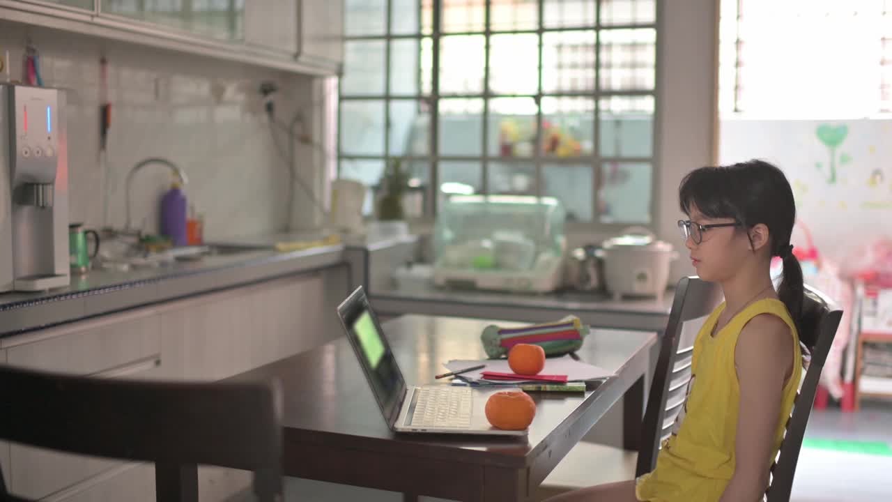 亚洲的中国女孩看着笔记本电脑的摄像头，拿着红包和橘子向她的祖父母祝贺春节