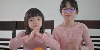 亚洲的中国小女孩和她的妹妹看着笔记本电脑的摄像头，用红包和橘子向她的祖父母祝贺春节