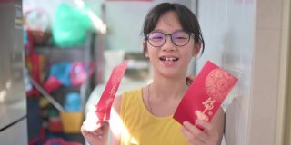 亚洲中国女孩看着手机摄像头，拿着红包和橘子向她的祖父母祝贺春节