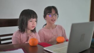 亚洲的中国小女孩和她的妹妹看着笔记本电脑的摄像头，用红包和橘子向她的祖父母祝贺春节视频素材模板下载
