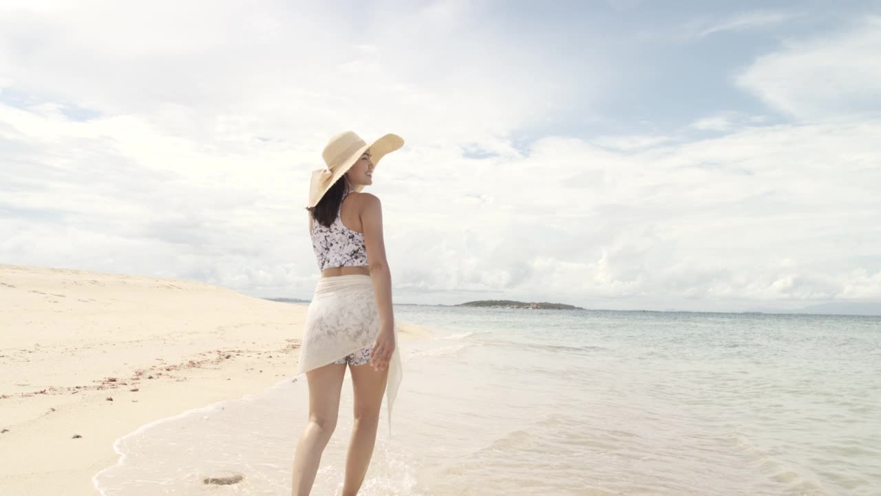 美丽年轻的亚洲女人走在海滩上。