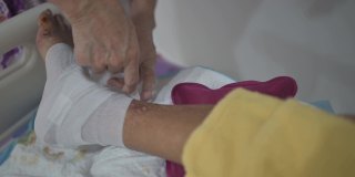 亚洲资深妇女包裹她因糖尿病和压疮伤卧床的丈夫的腿