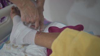 亚洲资深妇女包裹她因糖尿病和压疮伤卧床的丈夫的腿视频素材模板下载