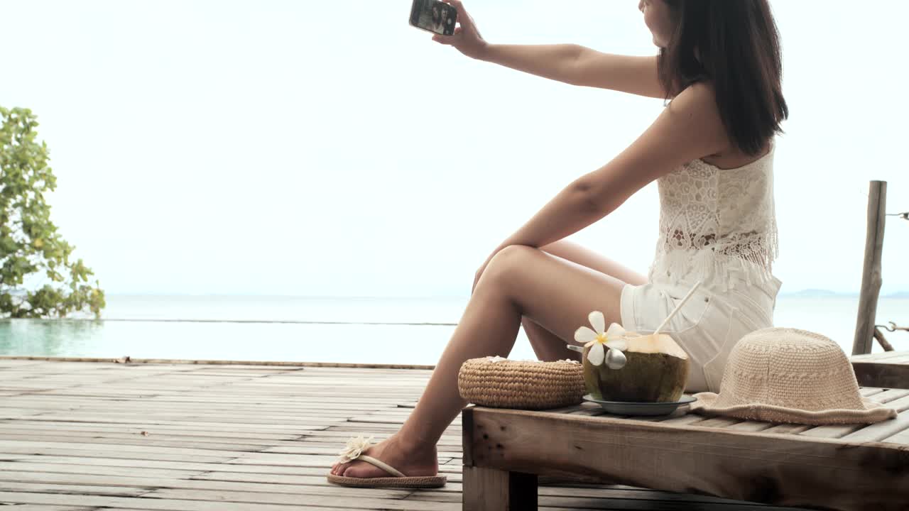 美丽年轻的亚洲女人喝椰子汁沿着海滩。