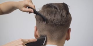 女孩美发师用剪子在男孩的鬓角和后脑勺上剪头发。