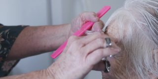 一个专业护理发型师在剪一个年长的白人妇女的刘海期间在家理发的近距离手持式拍摄