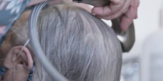 手持拍摄的专业护理发型师洗一个年长的白人妇女的白色和灰色的头发在厨房水槽在洗头设置在家里