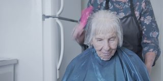 手持拍摄的一个年长的白人妇女在家里理发由专业护理发型师