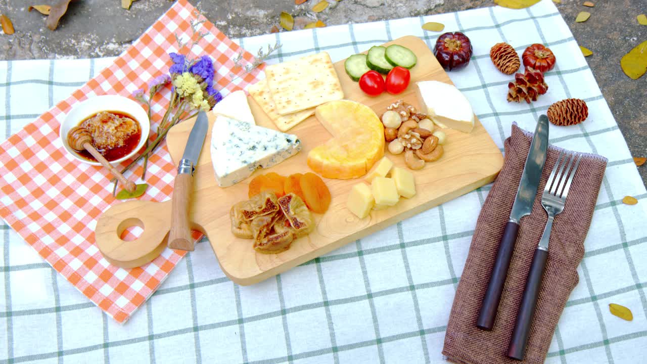 什锦奶酪和熟食拼盘组成的Camembert，蓝色和豪达，混合干果，坚果在热带花园的背景。