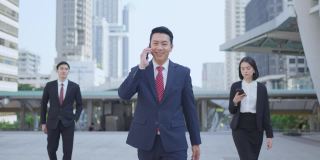 亚洲经理聪明的商人使用智能手机在城市。那人拿着电话，一边说话，一边微笑着站在户外。以电信和移动网络为经营理念。